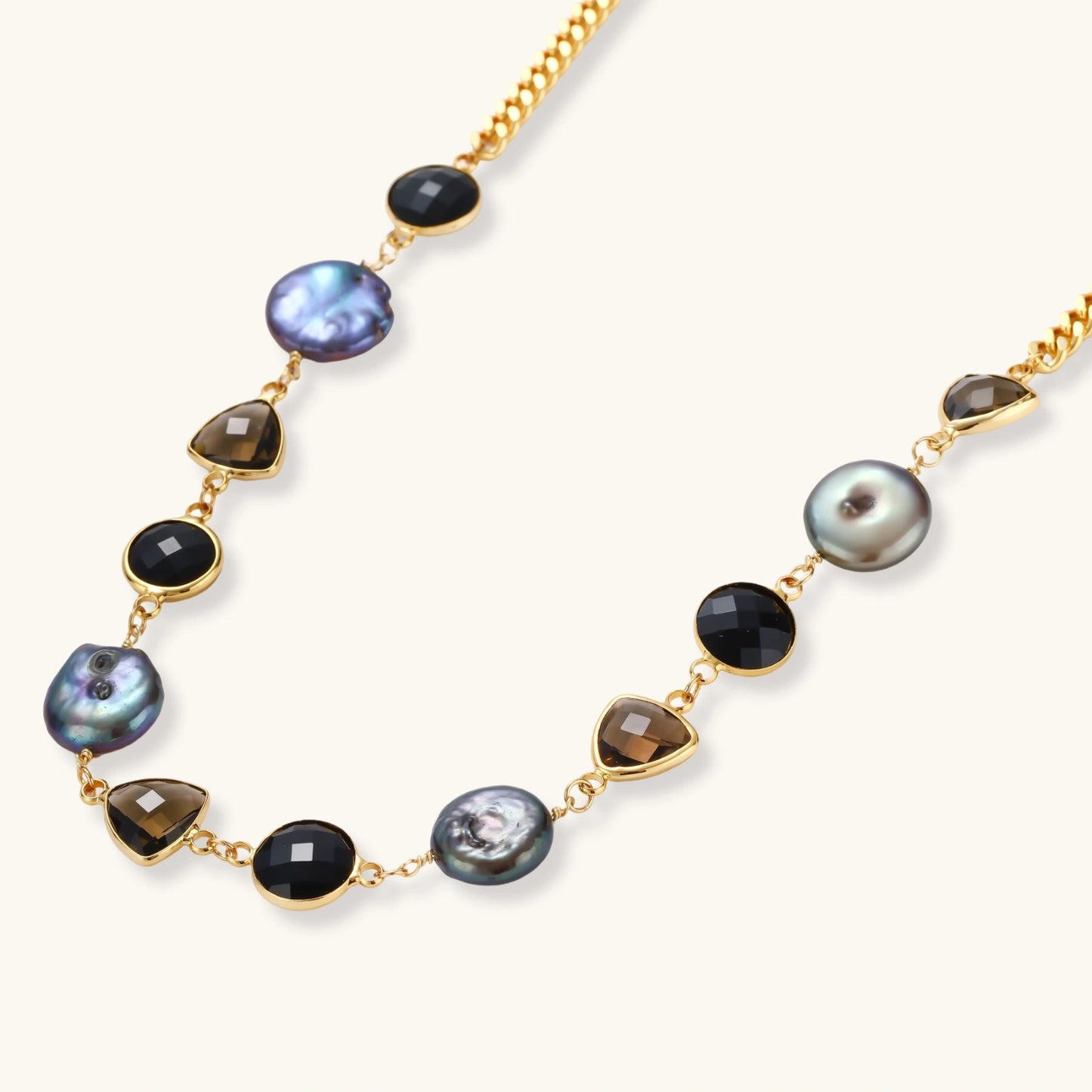 18k gold-plated chain necklace featuring lustrous baroque pearls, black onyx rounds, and smoky quartz triangular stones on white background.