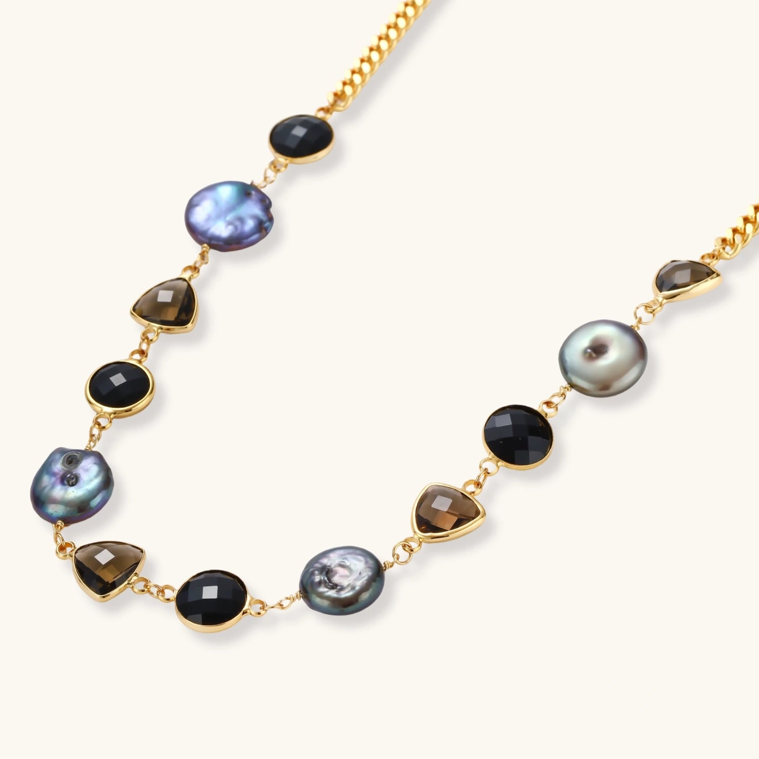 18k gold-plated chain necklace featuring lustrous baroque pearls, black onyx rounds, and smoky quartz triangular stones on white background.