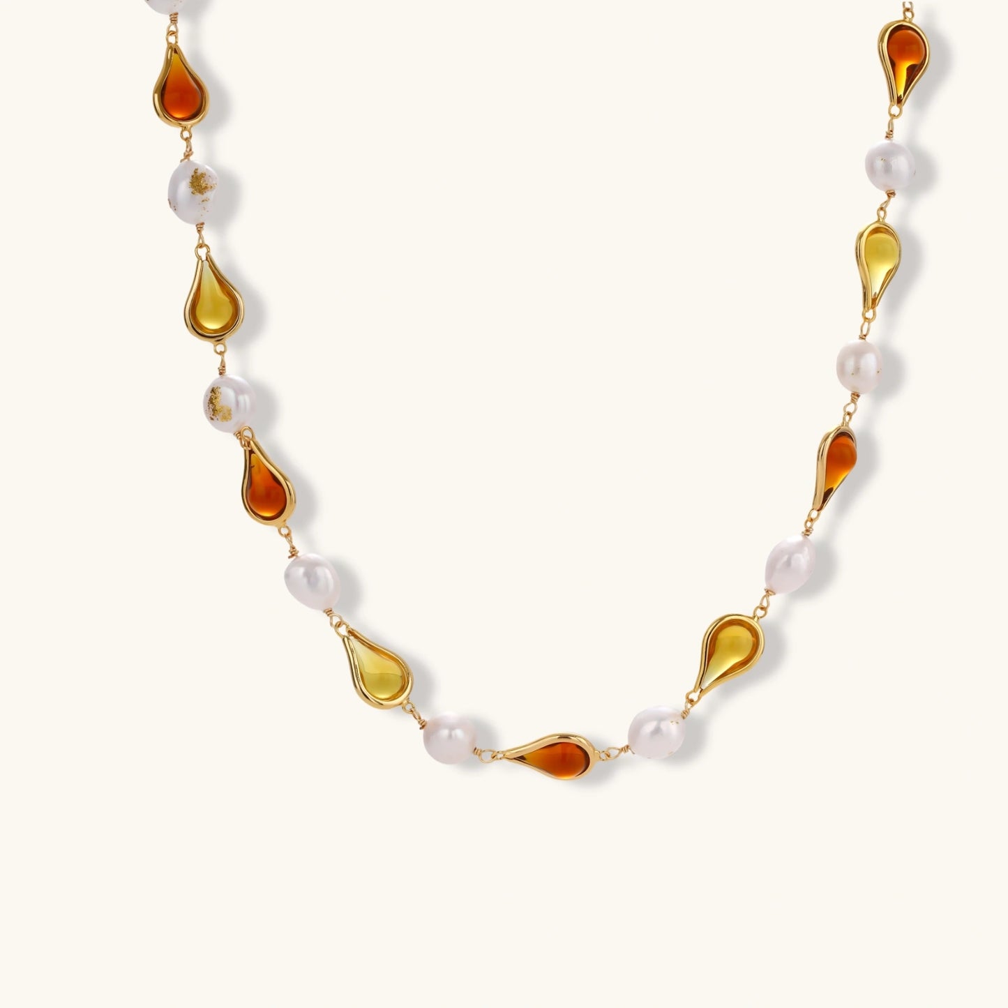 Gold-plated copper necklace with amber teardrop settings and white baroque freshwater pearls on cream background.