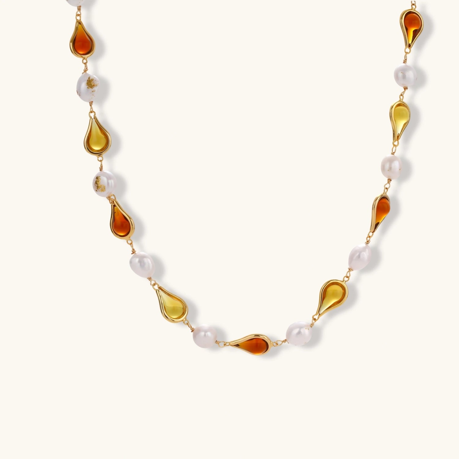 Gold-plated copper necklace with amber teardrop settings and white baroque freshwater pearls on cream background.
