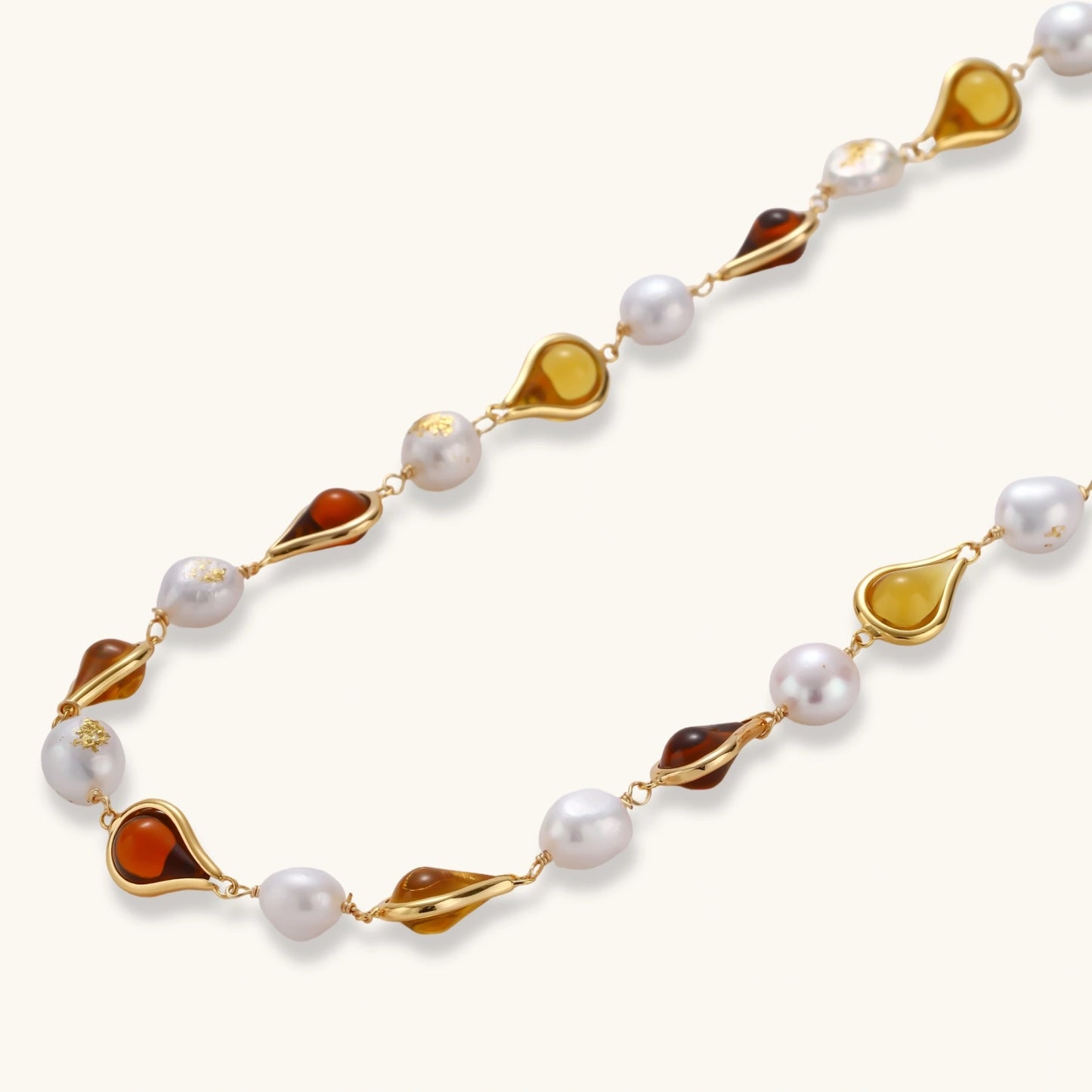 Gold-plated copper necklace with amber teardrop settings and white baroque freshwater pearls on cream background.