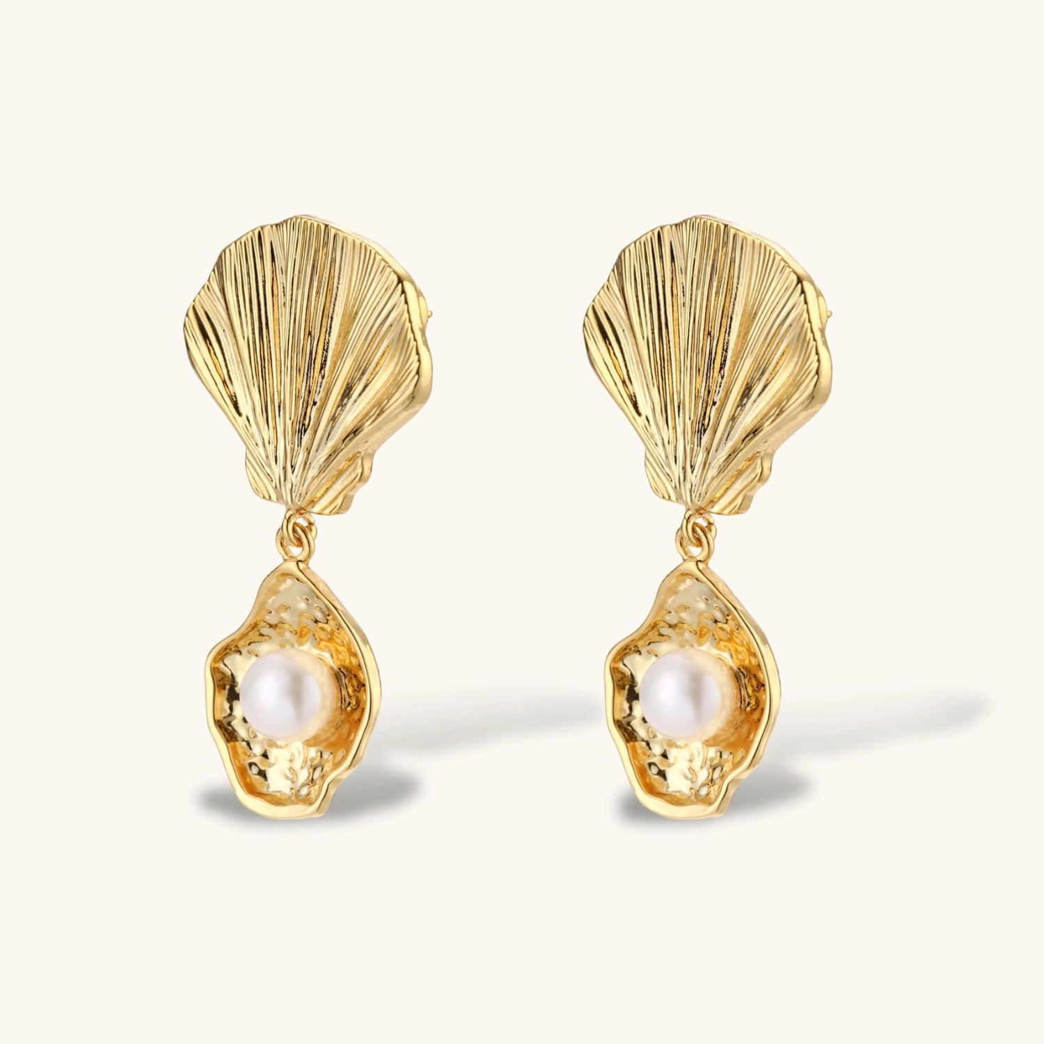 Gold shell-shaped drop earrings with scallop tops and oyster bottoms featuring round freshwater pearls on white background.